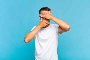 young handsome man covering face with both hands saying no to the camera! refusing pictures or...