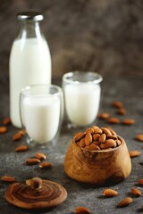 Almond milk in glass with almonds nuts on grey concrete background. Vegan food.
