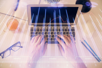 Double exposure of man's hands typing over laptop keyboard and forex chart hologram drawing. Top view. Financial markets concept.