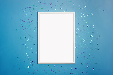 Festive background with blank white photo frame on blue with scattered confetti. Mock up for photo or text. Top view. Flat lay style.