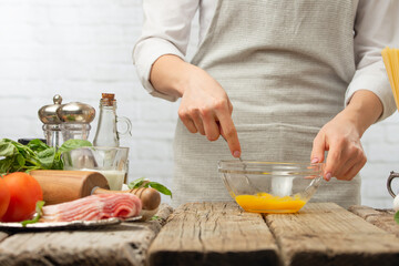 Chef in white uniform whips the yolk by fork in glass bowl for cooking pasta alla carbonara. Backstage of preparing traditional italian dish on white background. Frozen motion. Recipe book.