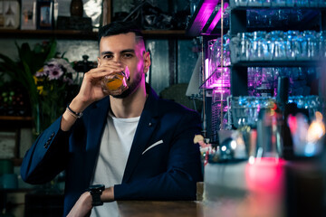 Portrait handsome Caucasian man sitting at bar counter holding whiskey glass with ice and enjoy drinking tasty alcoholic drink from barman in nightclub. Nightlife party celebration and holiday concept