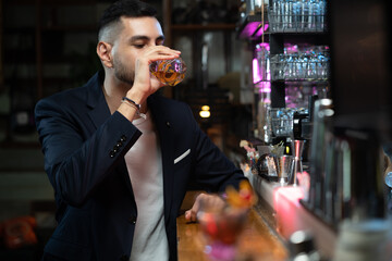 Portrait handsome Caucasian man sitting at bar counter holding whiskey glass with ice and enjoy...