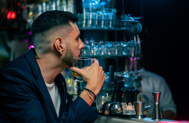 Portrait handsome Caucasian man sitting at bar counter holding whiskey glass with ice and enjoy drinking tasty alcoholic drink from barman in nightclub. Nightlife party celebration and holiday concept