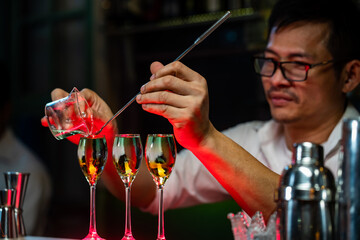 Professional barman pouring liquor into cocktail glass on counter bar for serve to customer in nightclub party. Male mixologist bartender preparing mixed alcoholic drink for customer at bar