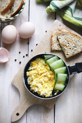 Scrambled eggs in pan with cucumber top view