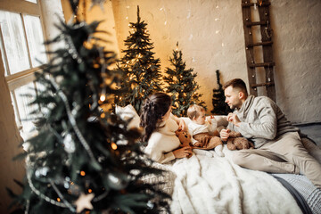 Fototapeta na wymiar Lovely parents with little daughter lay at the bed near decorated Christmas tree, smiling, enjoy happy moments together, new year celebration, cozy winter holidays concept