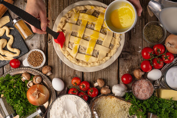 Chef hands eggs the raw pie on wooden table with variety of ingredients background. Concept of cooking process. Backstage of preparing tasty meal. View from above. frozen motion. Dish from recipe book