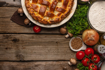 Appetizing meat pie on wooden table with variety of ingredients background. Concept of cooking process. Backstage of preparing tasty meal. View from above. Flat lay. Recipe book. Space for text.