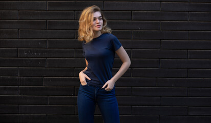 Young blonde woman in blue t-shirt on the background brick wall