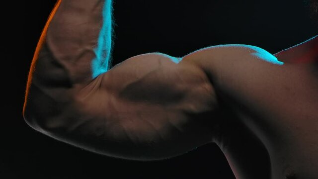 Professional athlete bodybuilder flexes the biceps on the arm, showing strong muscles. The concept of sports and body. Picture taken in the studio on a black background. Slow motion. Close up.