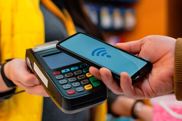 Customer is paying with smartphone in shop using NFC technology. against the background of the...