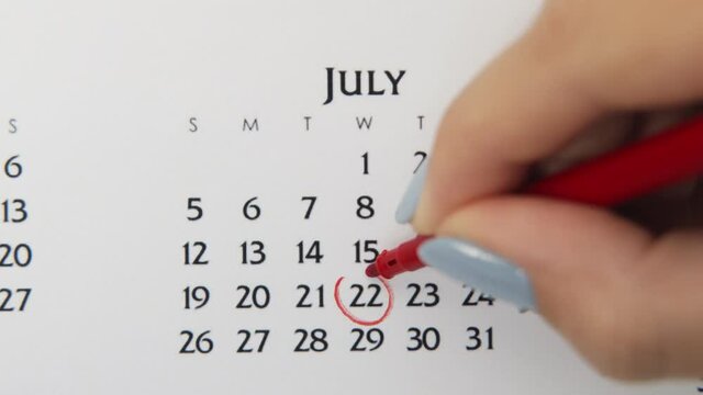 Female hand circle day in calendar date with a red marker. Business Basics Wall Calendar Planner and Organizer. July 22th