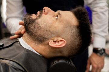 Client lying on a barber's chair while the barber pours shaving cream