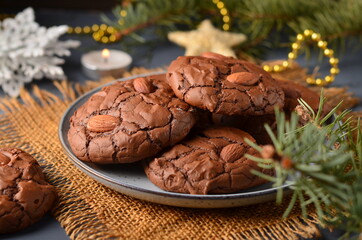 Chocolate cookies with almonds are on a plate, festive surroundings.