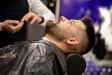 Client lying on a barber's chair while the barber pours shaving cream
