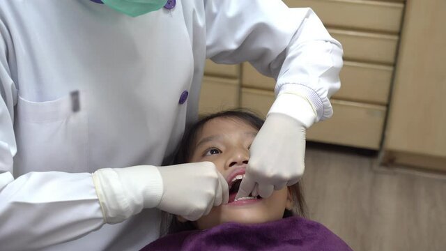 dentist using dental floss to clean food from tooth of asian girl 