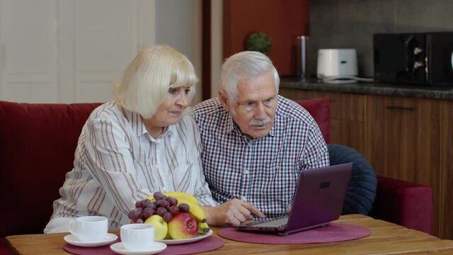 Happy senior elderly couple grandfather and grandmother looking on digital laptop making online shopping and celebrating. Mature old husband and wife watching news videos, using social media at home