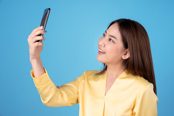 Happy young Asian woman taking a selfie with a smartphone, Isolated on a blue background.