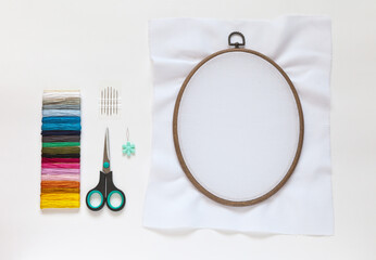 Needlework and embroidery. Accessories: needles, set of colored mouline threads, needle threader, scissors and cotton canvas on oval  hoop for stitch or cross-stitch embroidery. Copy space, flat lay © Katvic