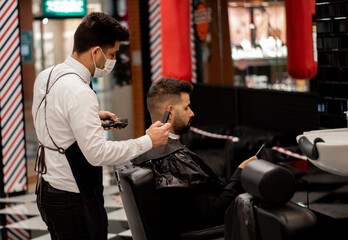 wide shot of an elegant barber with a mask cuts the hair of a client with caucasian features