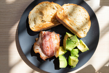 Breakfast plate consists of sourdough bread, bacon, and avocado.