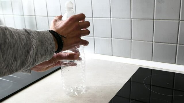Hands of a man crushing a plastic bottle. Empty container of water compressed for recycling. Garbage recycling concept in a kitchen. Background blurred voluntarily.