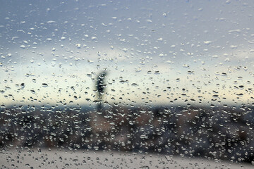 person in rain viewed through water droplets on the glass