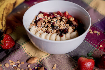 Delicious oatmeal with banana, strawberries, granola, blueberry, coconut and almonds on top, inside a white plate.