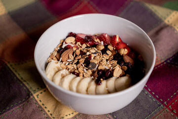 Delicious oatmeal with banana, strawberries, granola, blueberry, coconut and almonds on top, inside a white plate.