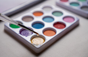 Naklejka premium Colored watercolors on a table and up a brush with water dripping in close up concept.