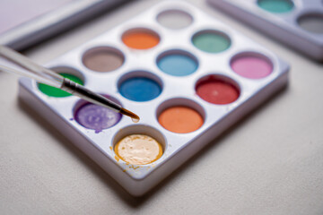 Colored watercolors on a table and up a brush with water dripping in close up concept.