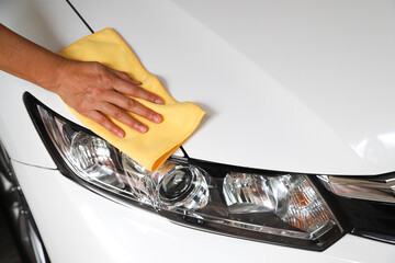 Closeup of white car cleaning  with yellow microfiber cloth by woman's hand.