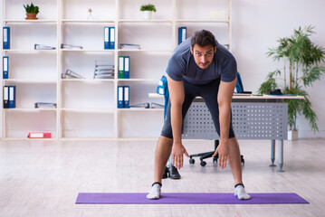 Young handsome employee doing sport exercises in the office