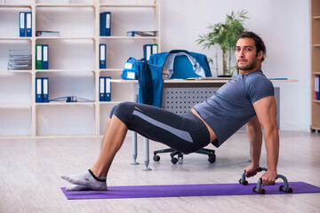 Fototapeta premium Young handsome employee doing sport exercises in the office