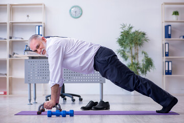 Aged male employee doing physical exercises during break