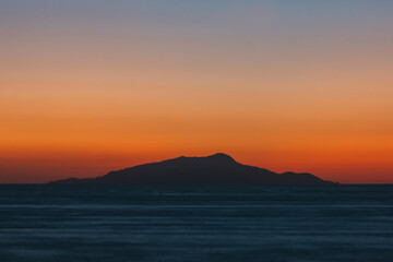 Fototapeta na wymiar Sunset behind Ischia Island with Slhouette, an Orange and Teal or Blue Abstract Background
