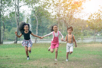 Group of young children happily  holding hands and running towards camera in park.