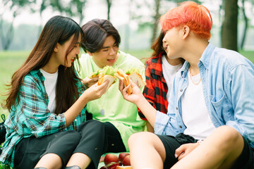 A group of young Asians happily eating sandwiches at the park