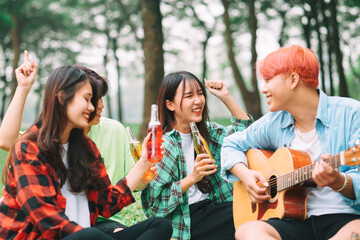 group of happy Asian young people sitting on the guitar and singing in the park