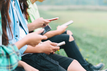 A cropped image of A group Asian friends are sitting using their smartphones and chatting in the park