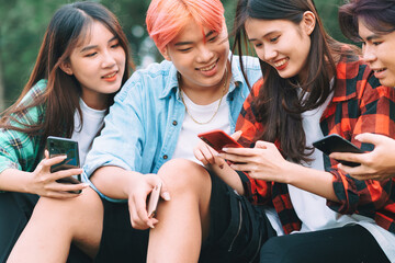 A group of happy Asian friends are sitting using their smartphones and chatting in the park