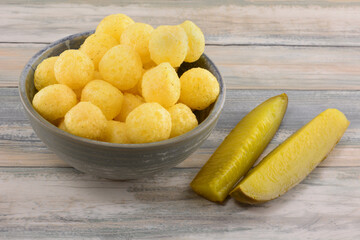 Dill pickle corn puffs in snack bowl with dill pickle spears in table