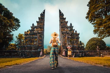 Poster Woman with backpack walking at big entrance gate in Bali, Indonesia. © Davide Angelini