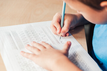 Close up of schoolboy doing writing task. Prewriting practice to prepare hand for write letters. Children education concept - obrazy, fototapety, plakaty