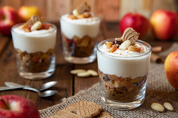 Kuchen im Glas mit Stücken vom Bratapfel, Zimt, Spekulatius, Apfel, Mandeln und Rosinen mit einer Creme aus Quark oder Mascarpone auf einem Tisch aus Holz in einer gemütlichen Küche zu Weihnachten