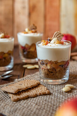 Kuchen im Glas mit Stücken vom Bratapfel, Zimt, Spekulatius, Apfel, Mandeln und Rosinen mit einer Creme aus Quark oder Mascarpone auf einem Tisch aus Holz in einer gemütlichen Küche zu Weihnachten