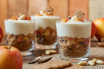 Kuchen im Glas mit Stücken vom Bratapfel, Zimt, Spekulatius, Apfel, Mandeln und Rosinen mit einer Creme aus Quark oder Mascarpone auf einem Tisch aus Holz in einer gemütlichen Küche zu Weihnachten