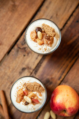 Kuchen im Glas mit Stücken vom Bratapfel, Zimt, Spekulatius, Apfel, Mandeln und Rosinen mit einer Creme aus Quark oder Mascarpone auf einem Tisch aus Holz in einer gemütlichen Küche zu Weihnachten