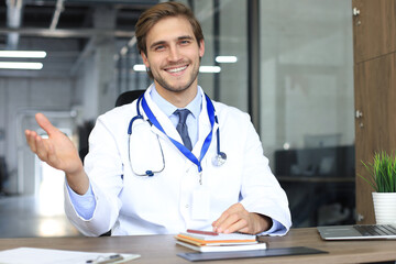 Smiling handsome male doctor talking at camera with patient.